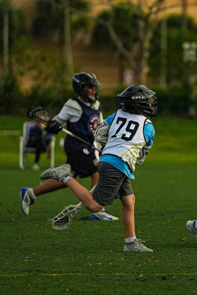 Two helmeted Redhawks boys running with sticks