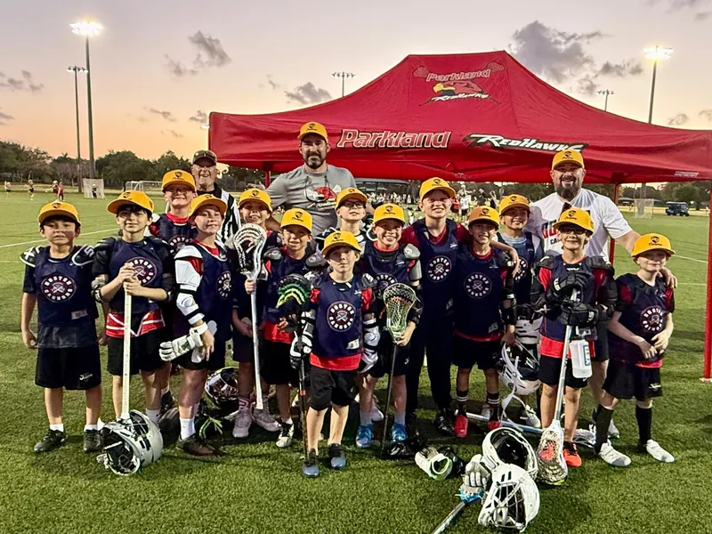 A Redhawks boys team and their coaches hold their sticks in front of the red Redhawks tent at sunset