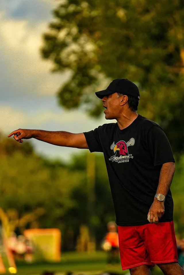 A Redhawks volunteer coach in a black Redhawks shirt points out a drill in golden evening light